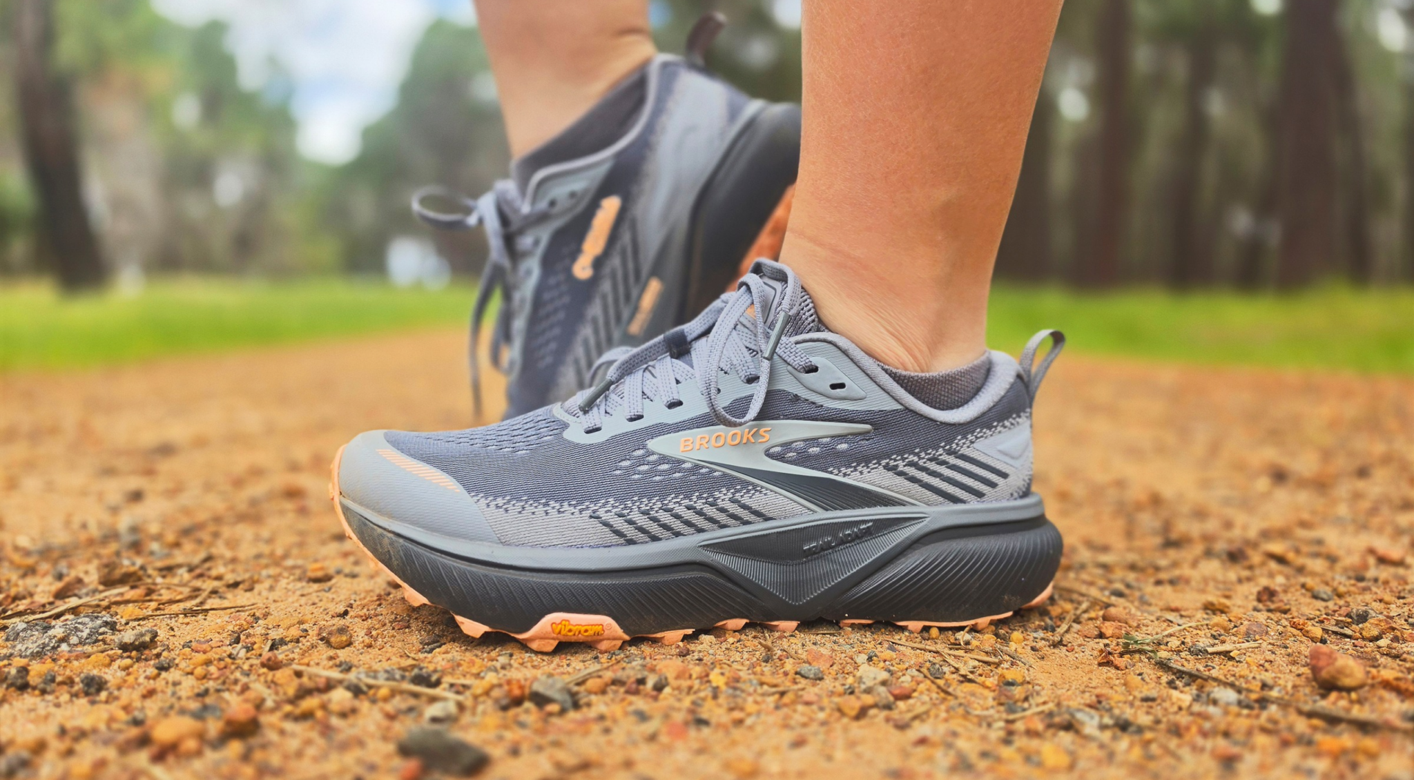 Grey Brooks Cascadia 20 trail running shoes worn on a dirt trail, showing the side profile and rugged outsole.