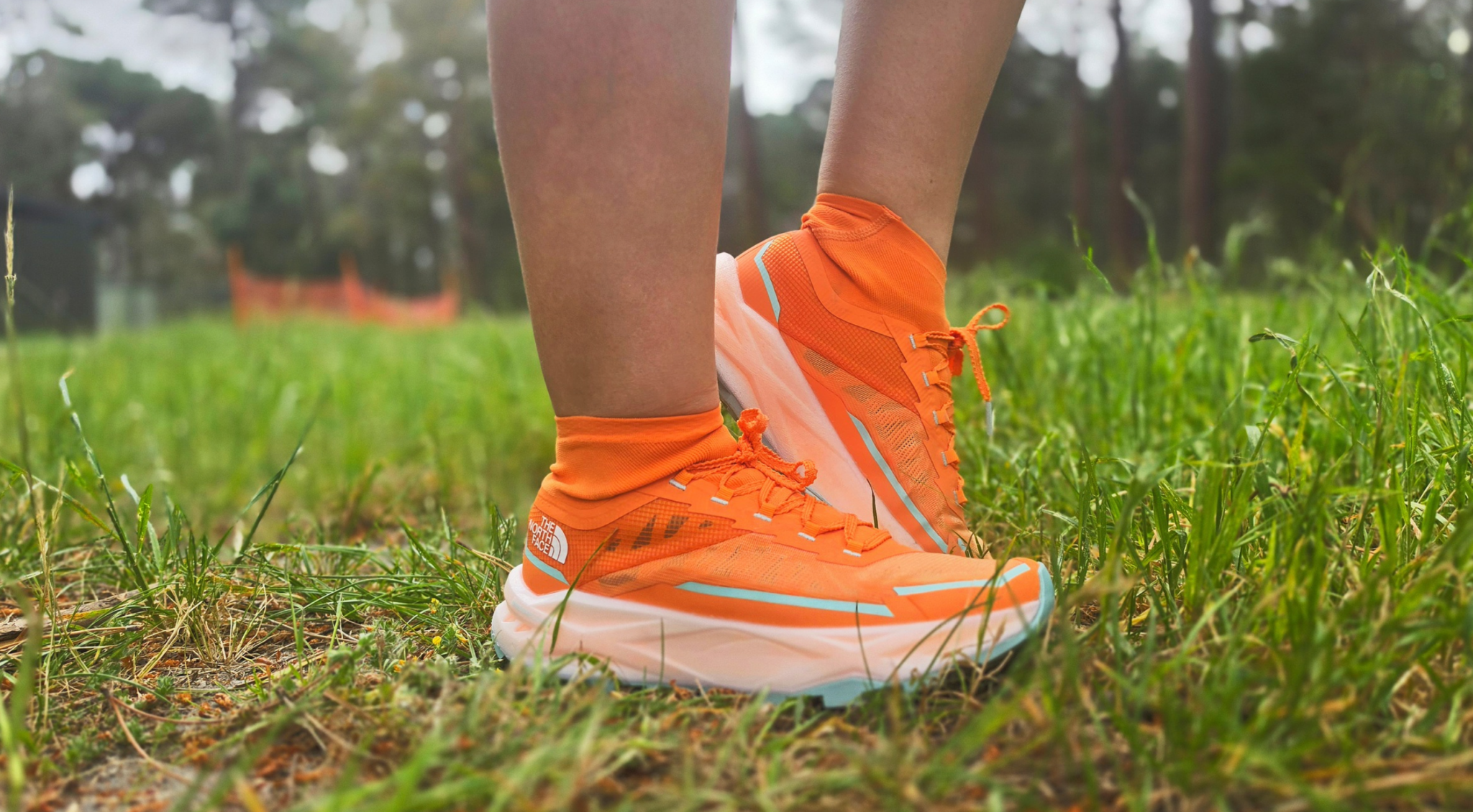 Bright orange The North Face Offtrail Ultra trail running shoes with integrated ankle gaiters, worn on a grassy trail.
